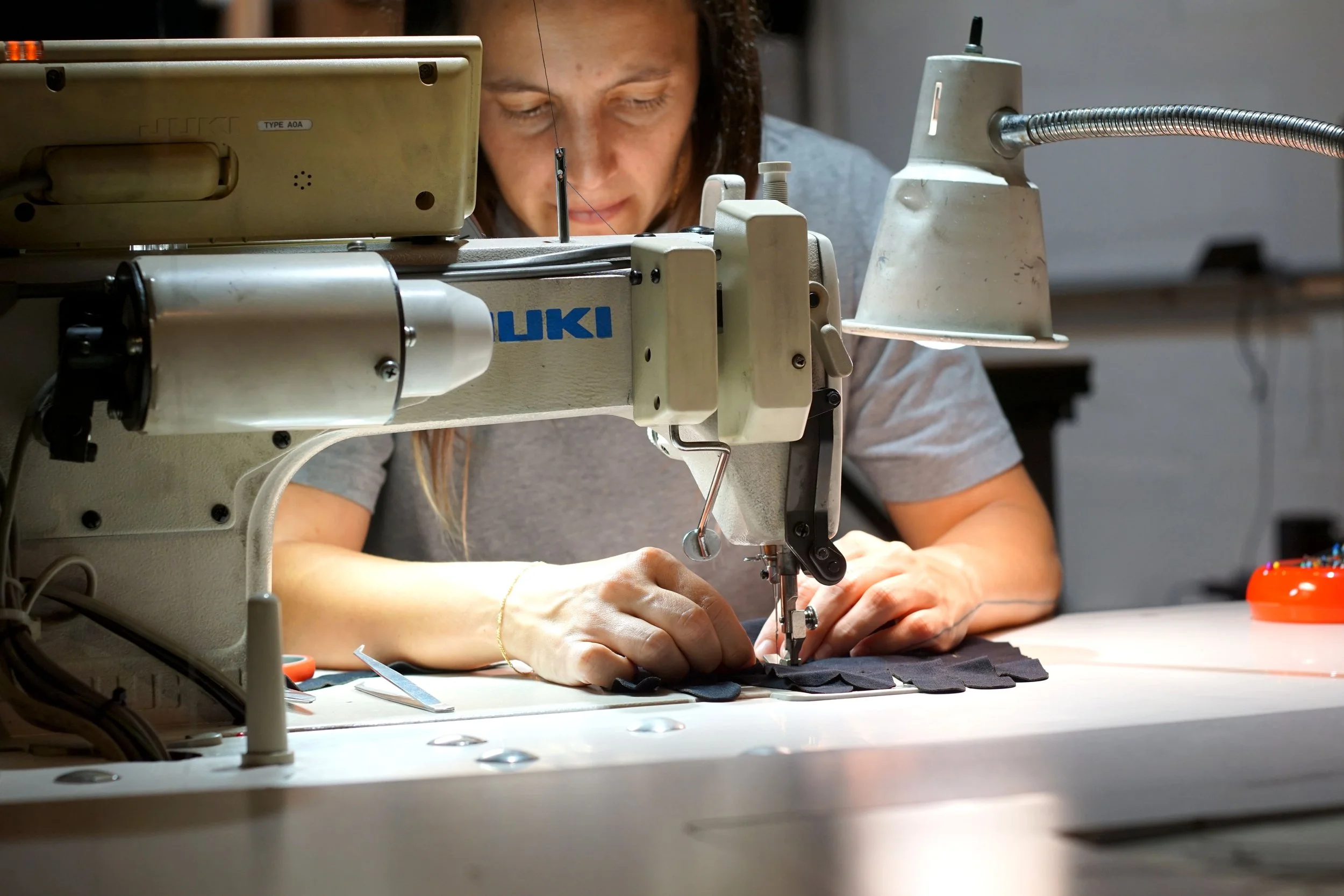 A woman sewing black fabric with a sewing machine in a workshop.