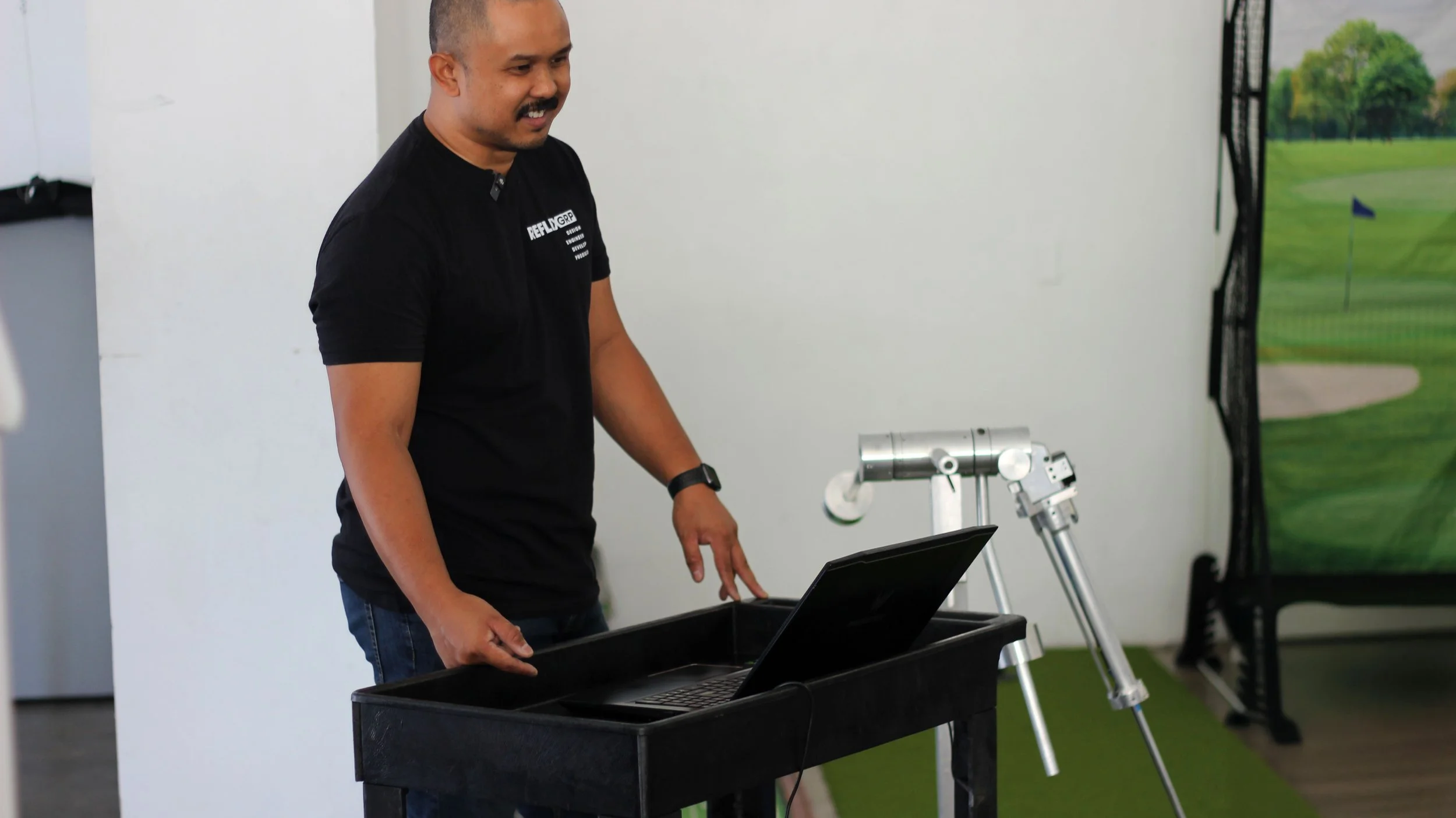 Man smiling at a laptop with a robotic arm and a golf course backdrop.